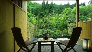 A wooden deck with two chairs and a table, overlooking a lush garden with a wooden fence and a stone lantern.