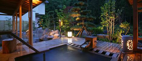 Un área de aguas termales con pasarelas de madera, una balsa de piedra y un farol.