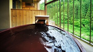 A wooden deck with a hot tub, a wooden fence, and a view of a forest.