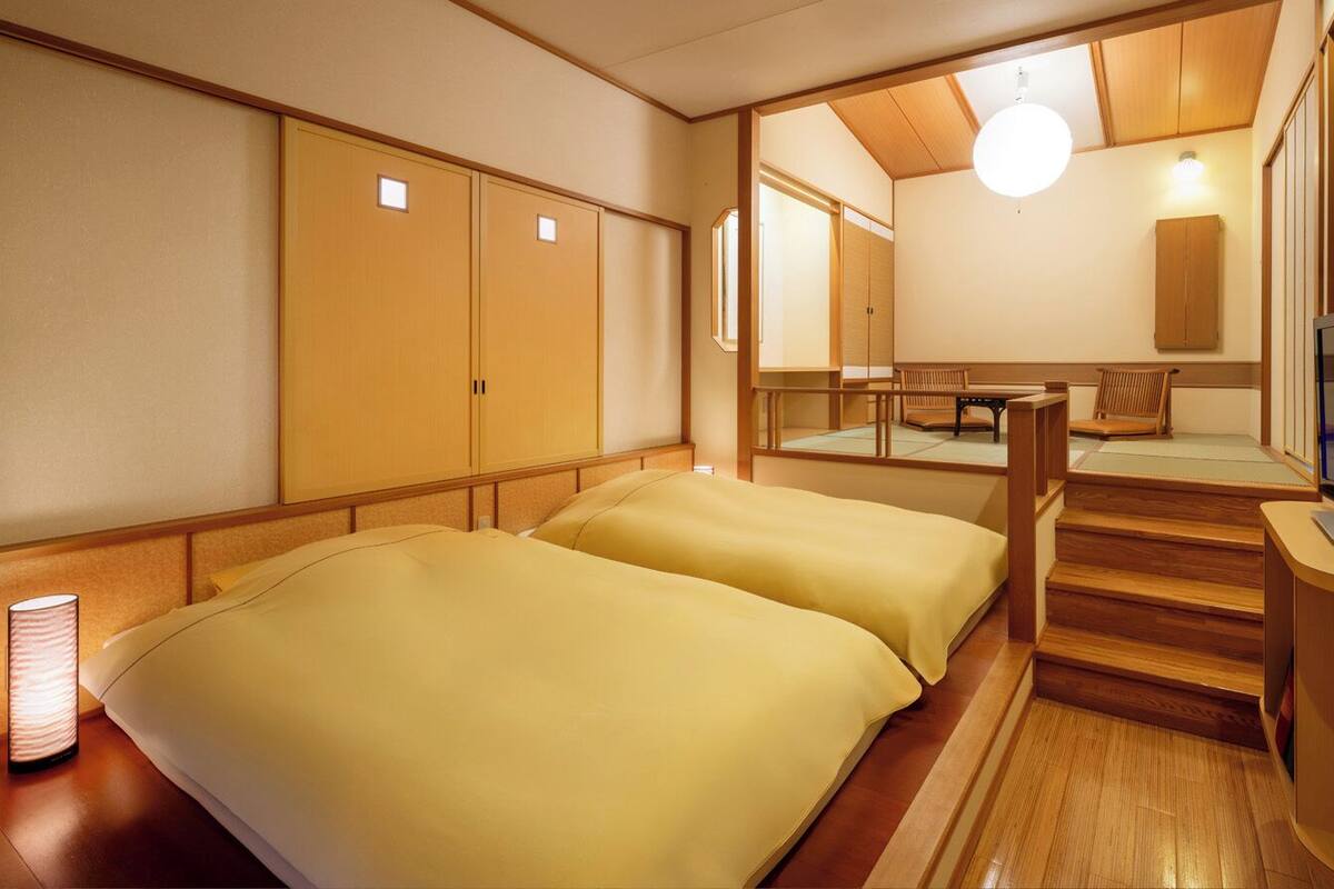 A hotel room with two beds, a TV, a wooden staircase, and a view of the outside.