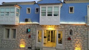 Un edificio de dos pisos con paredes de piedra y fachada azul, que presenta una entrada central con puertas de vidrio y un pequeño balcón arriba.