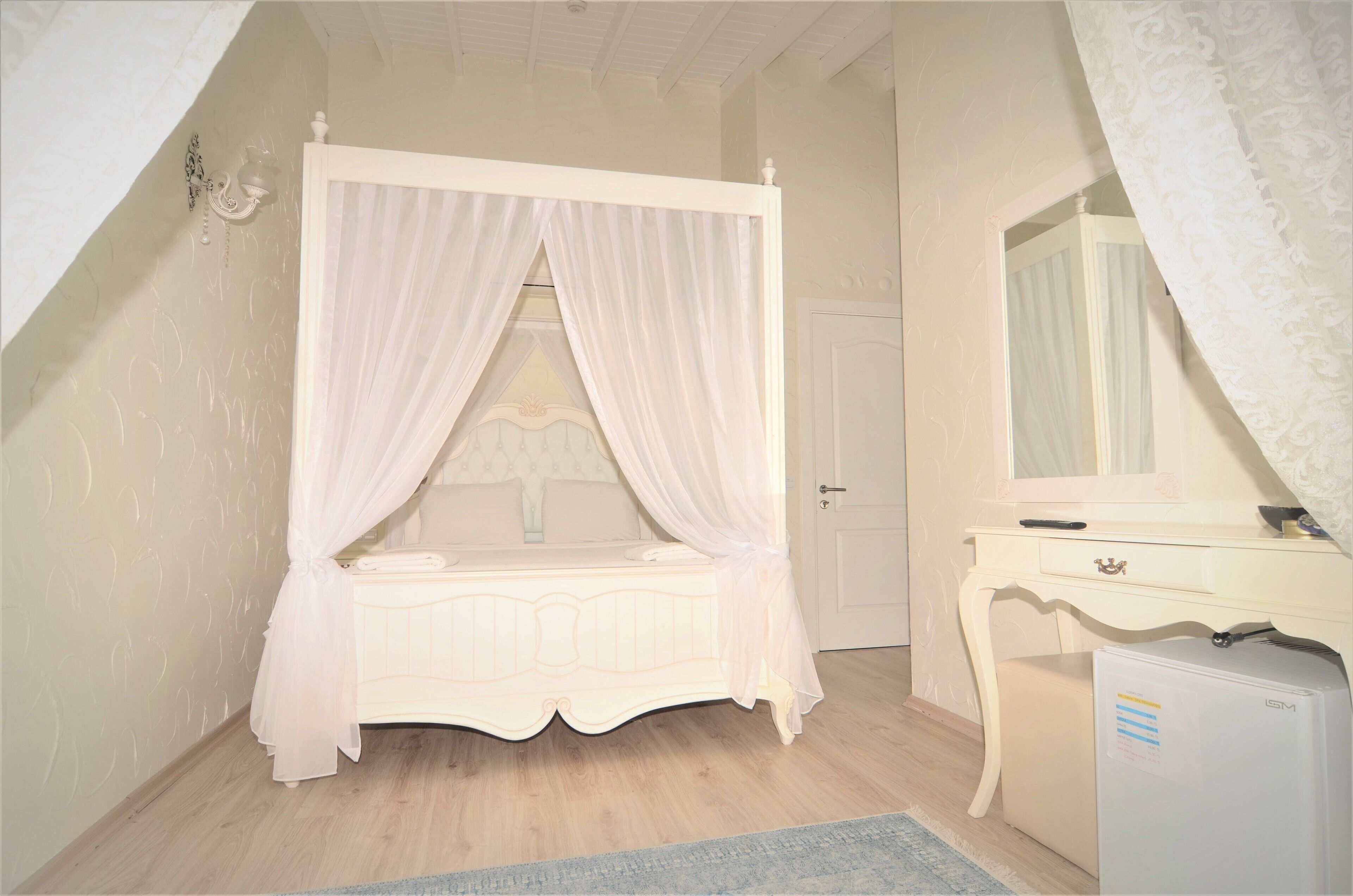 Ein Schlafzimmer mit einem Himmelbett, einem Schminktisch, einem Spiegel und einem kleinen Kühlschrank.