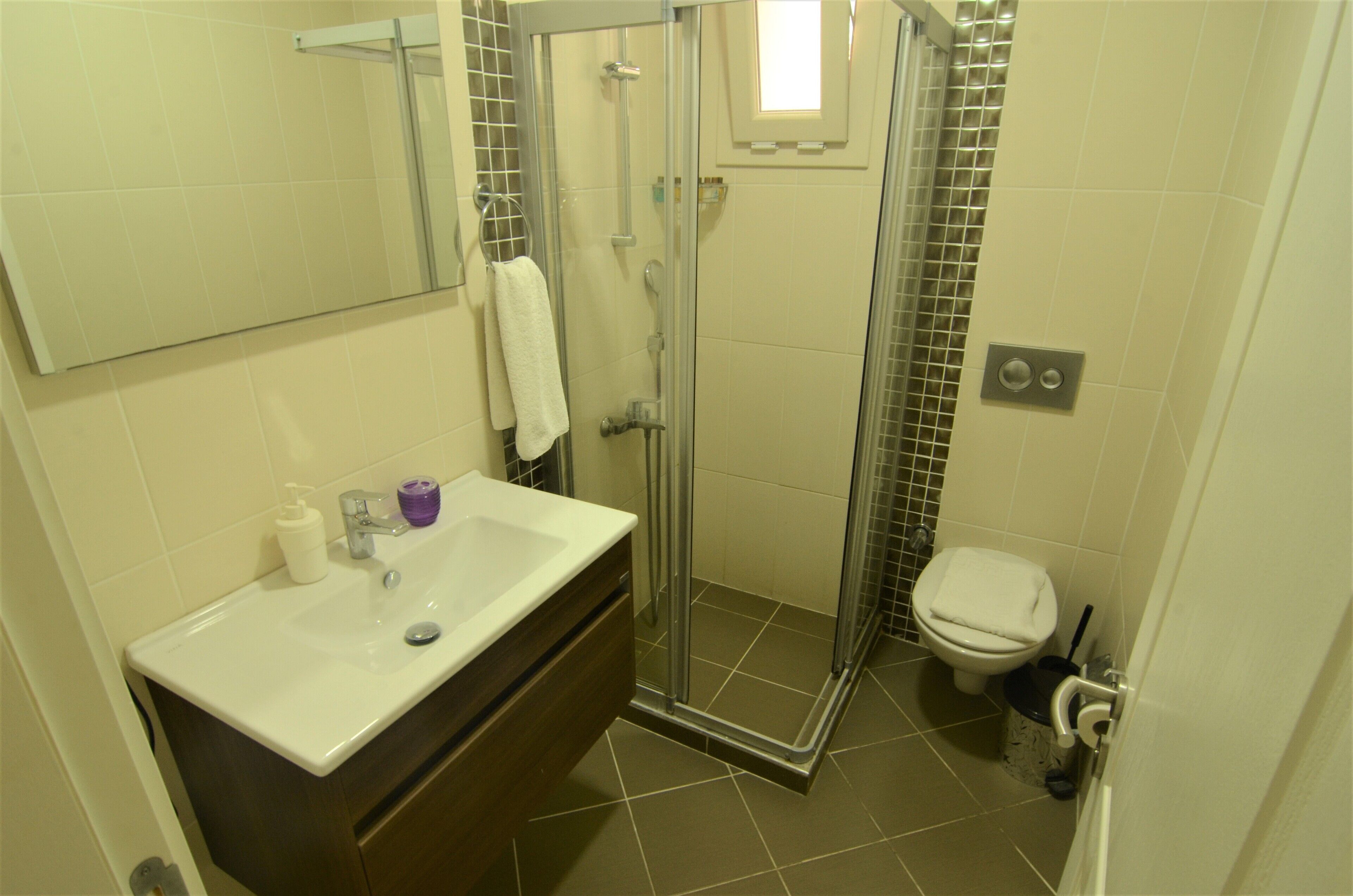 Un baño con cabina de ducha de vidrio, un lavabo blanco con espejo y un inodoro.