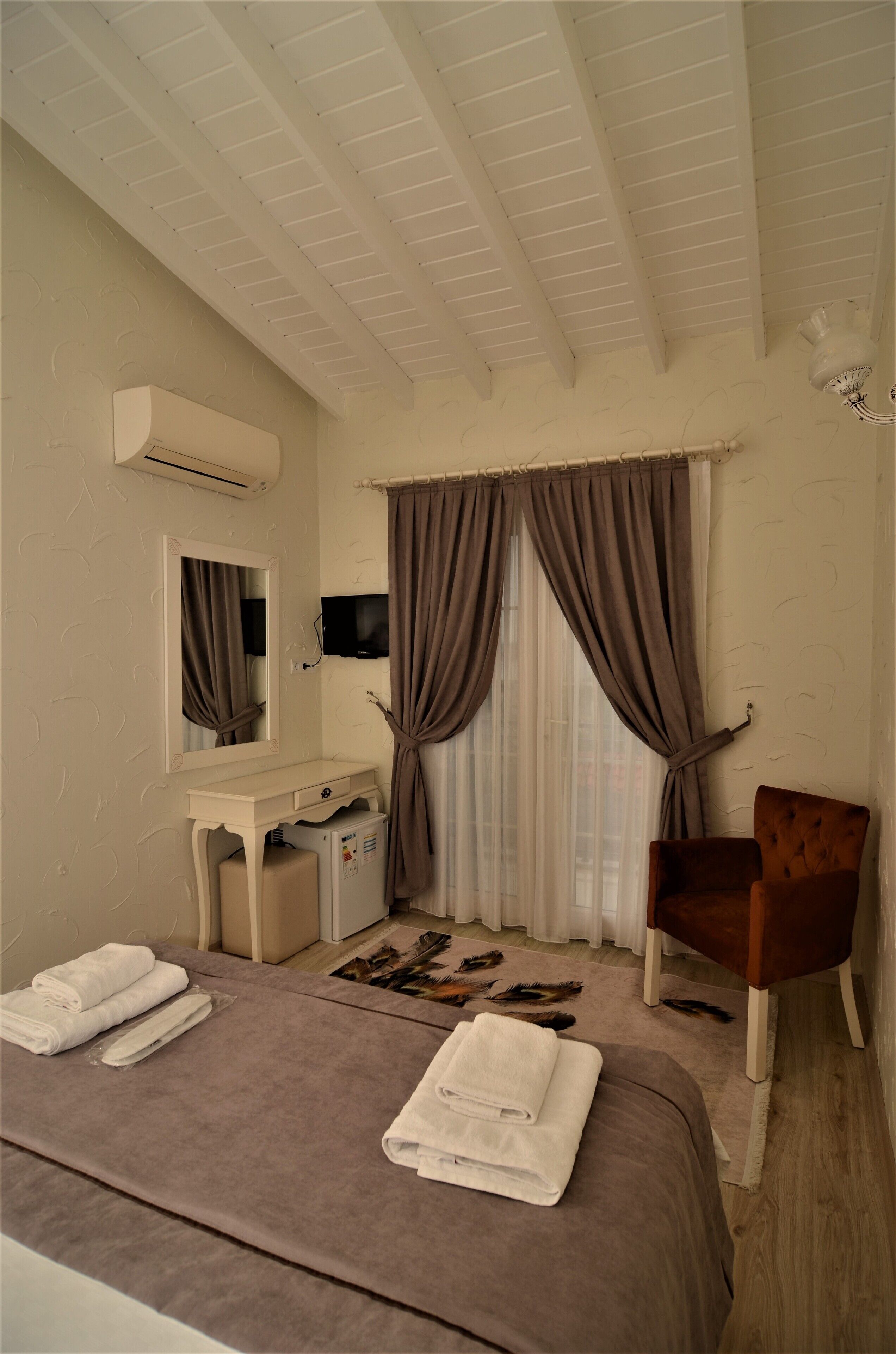 Un dormitorio con una cama, un tocador con espejo, una silla y un televisor en la pared.