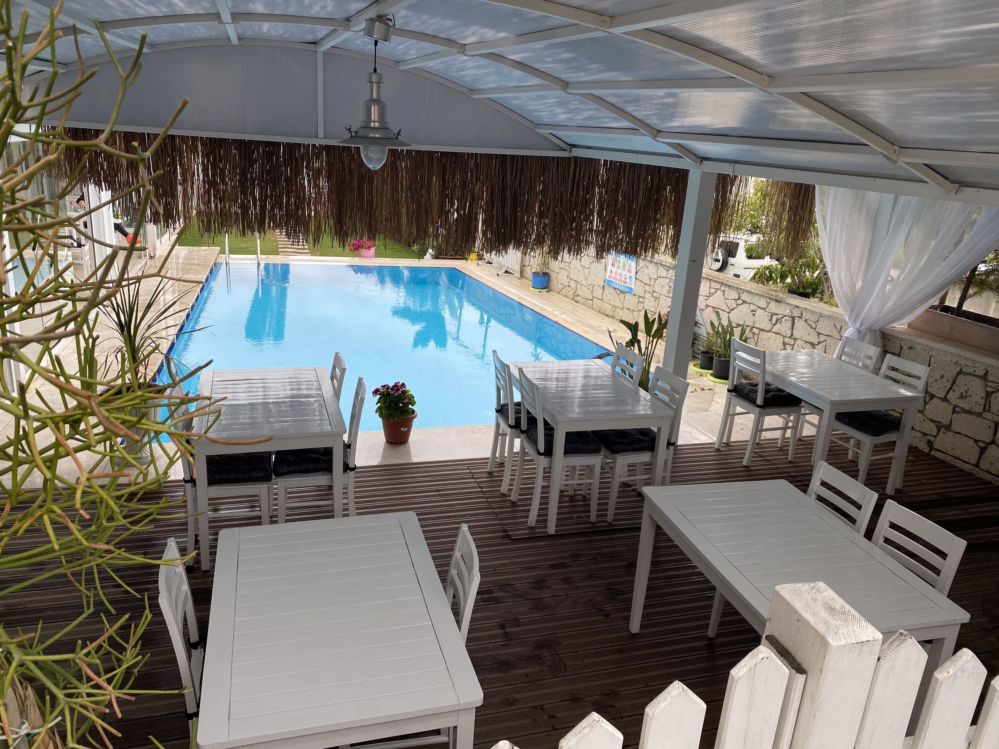 Un espace extérieur abrité, doté d’une piscine, de mobilier blanc et d’une pergola au-dessus.
