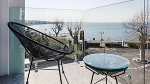 Een balkon met een stoel en tafel, met uitzicht op een wateroppervlak en een verre kustlijn.