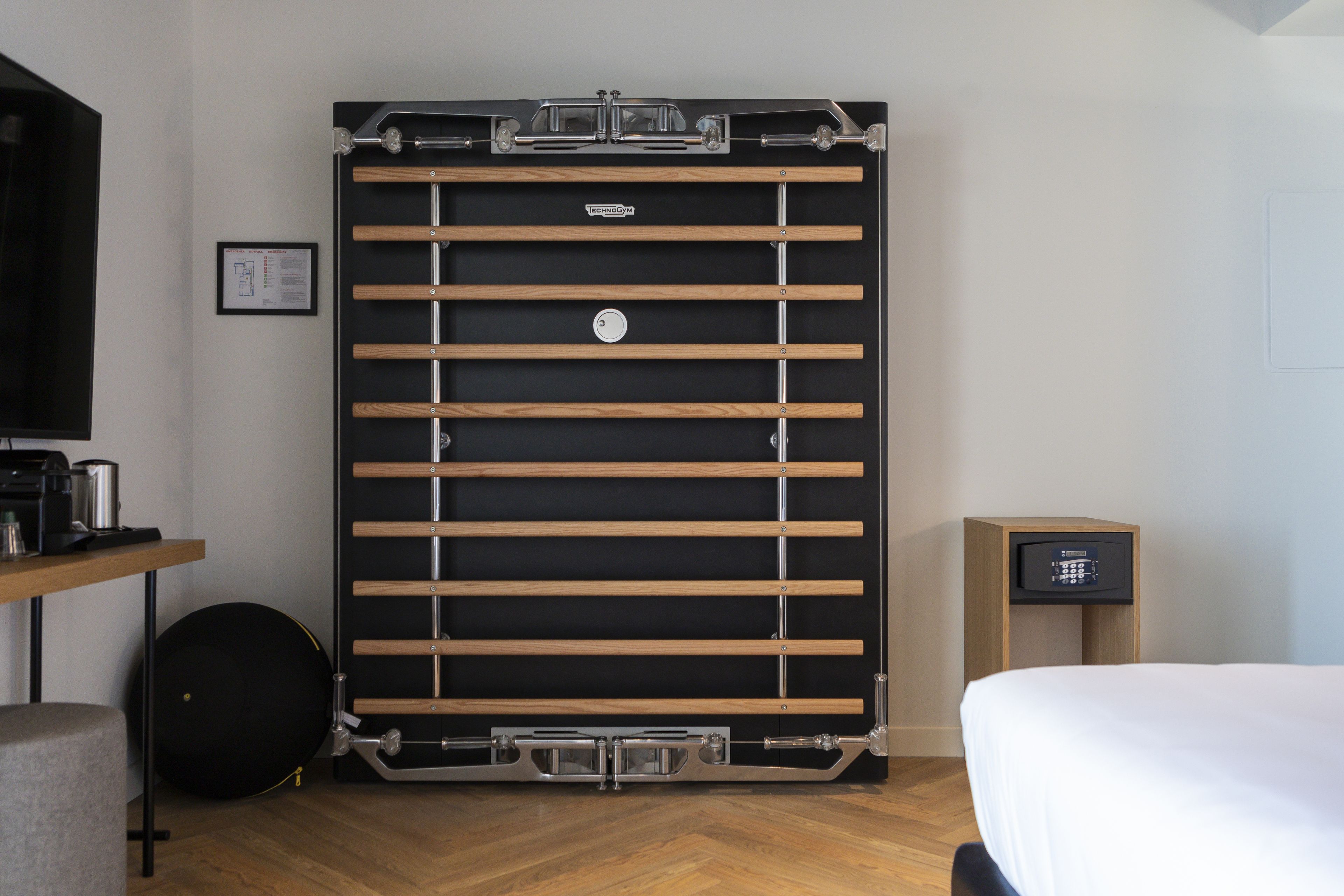 A compact room with a bed, a small desk, a wall-mounted TV, and a compact storage unit.