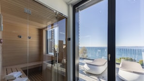 Een moderne sauna met glazen deuren, houten banken en uitzicht op zee door grote ramen.