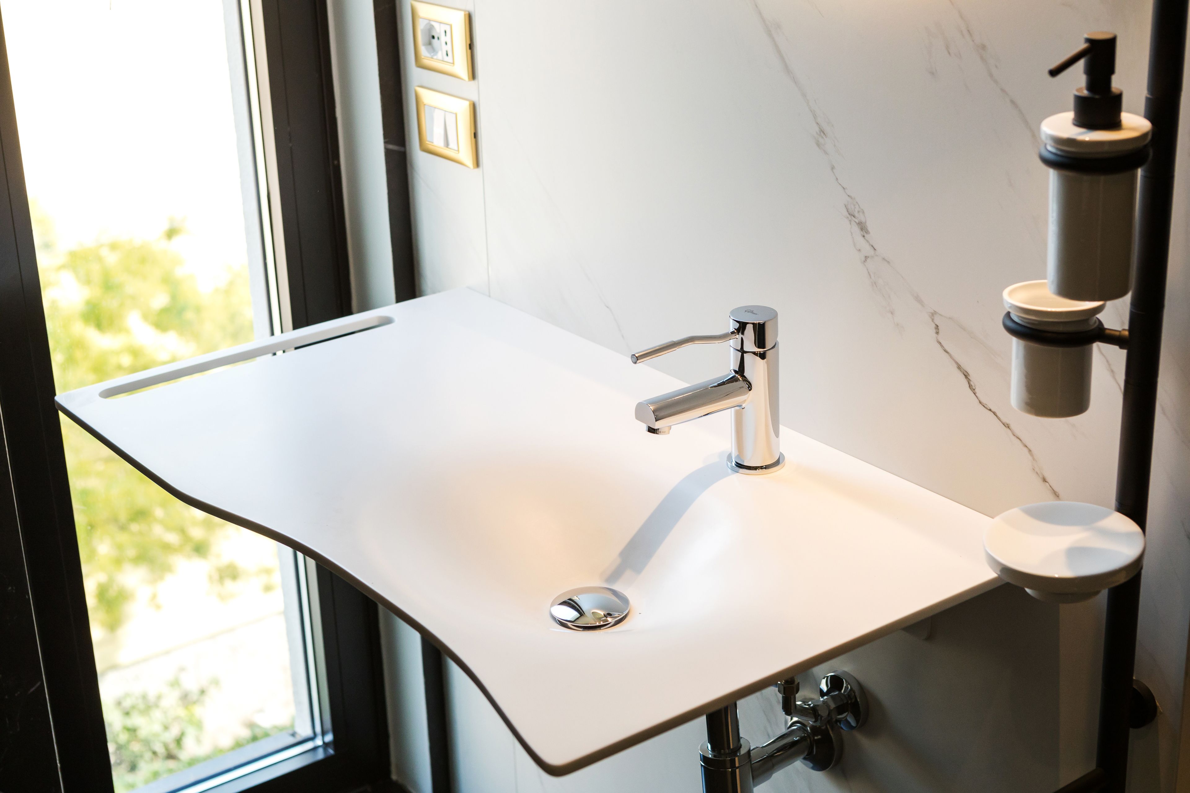 A modern bathroom with a white sink, chrome faucet, and a soap dispenser.