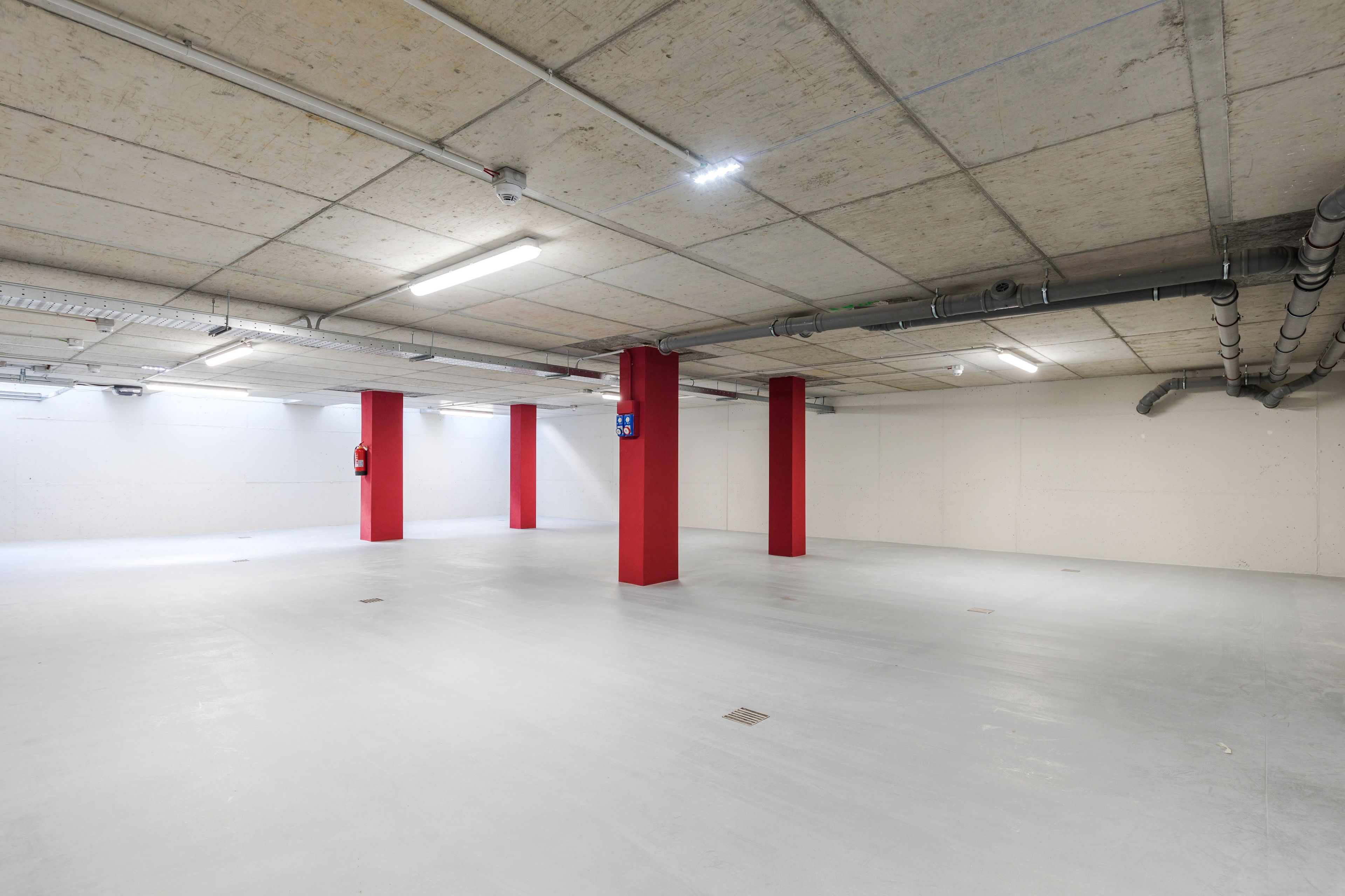 A spacious indoor parking area with concrete floors and red pillars.