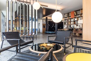 A modern lounge area with black leather chairs, a round glass table, and a bookshelf filled with books.