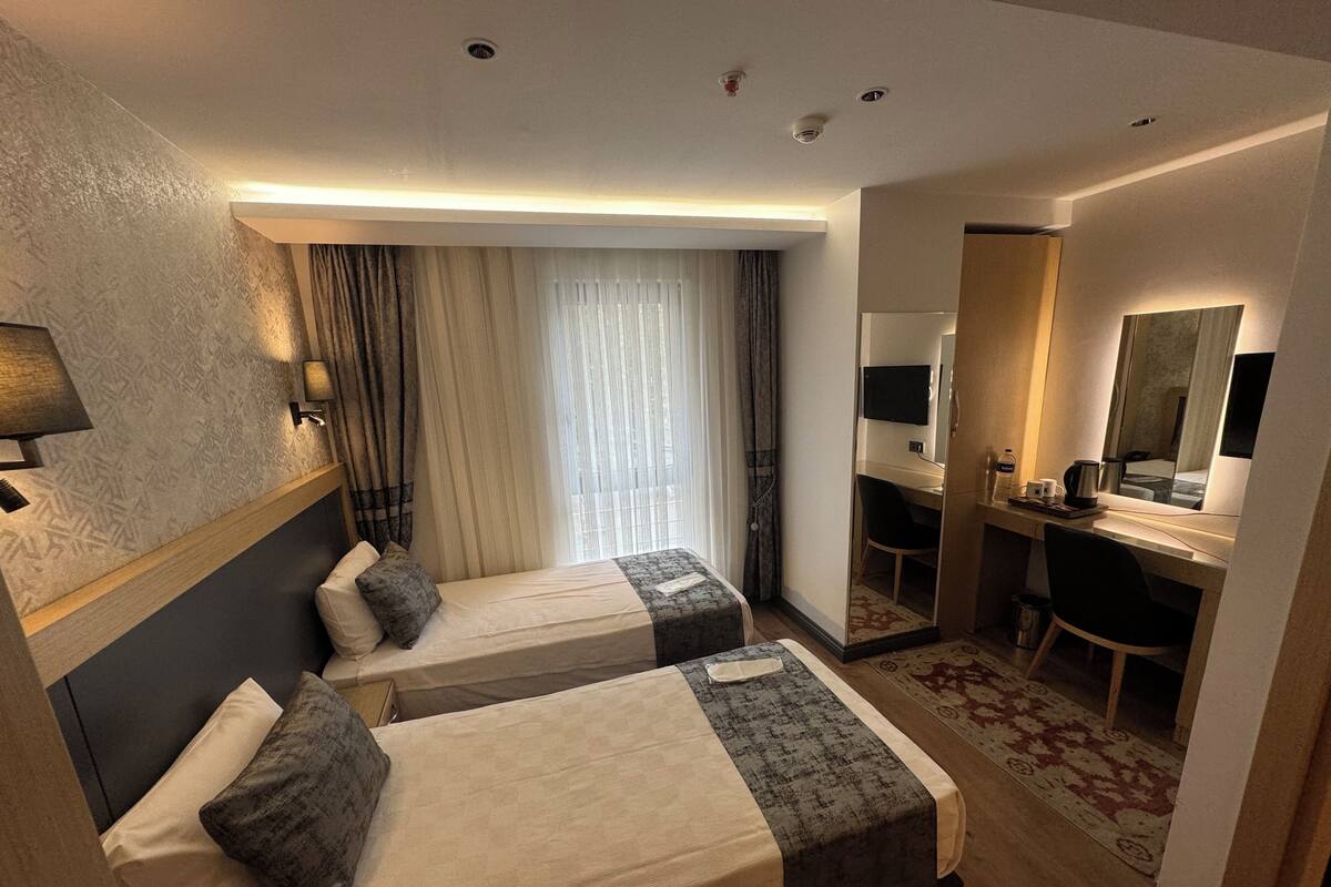 A hotel room with two beds, a desk, a chair, a mirror, and a television.