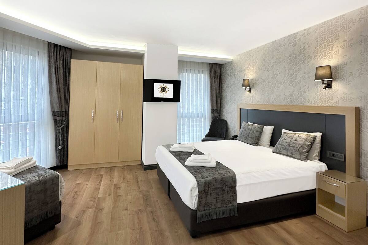 A modern hotel room with a large bed, a desk, a wardrobe, and a seating area.
