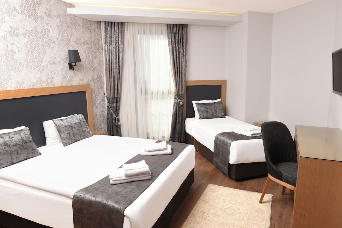 A hotel room with two beds, a desk, a chair, and a large window with curtains.