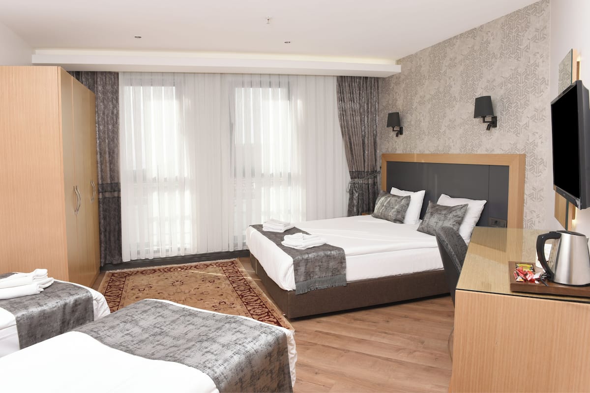 A hotel room with a large bed, two bedside tables, a desk with a kettle, and a TV.