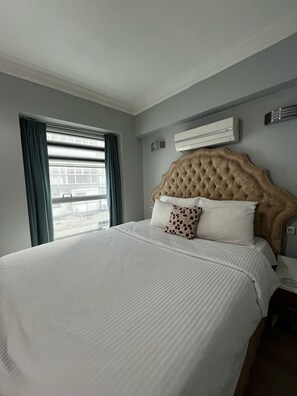 Een hotelkamer met een groot bed, een raam met gordijnen, een airconditioning en een nachtkastje.