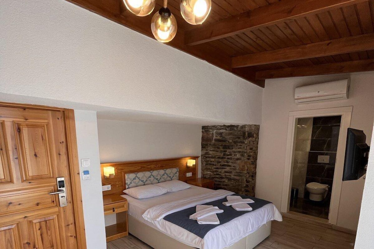 A bedroom with a wooden ceiling, a bed with white linens, a stone wall, and a wooden floor.