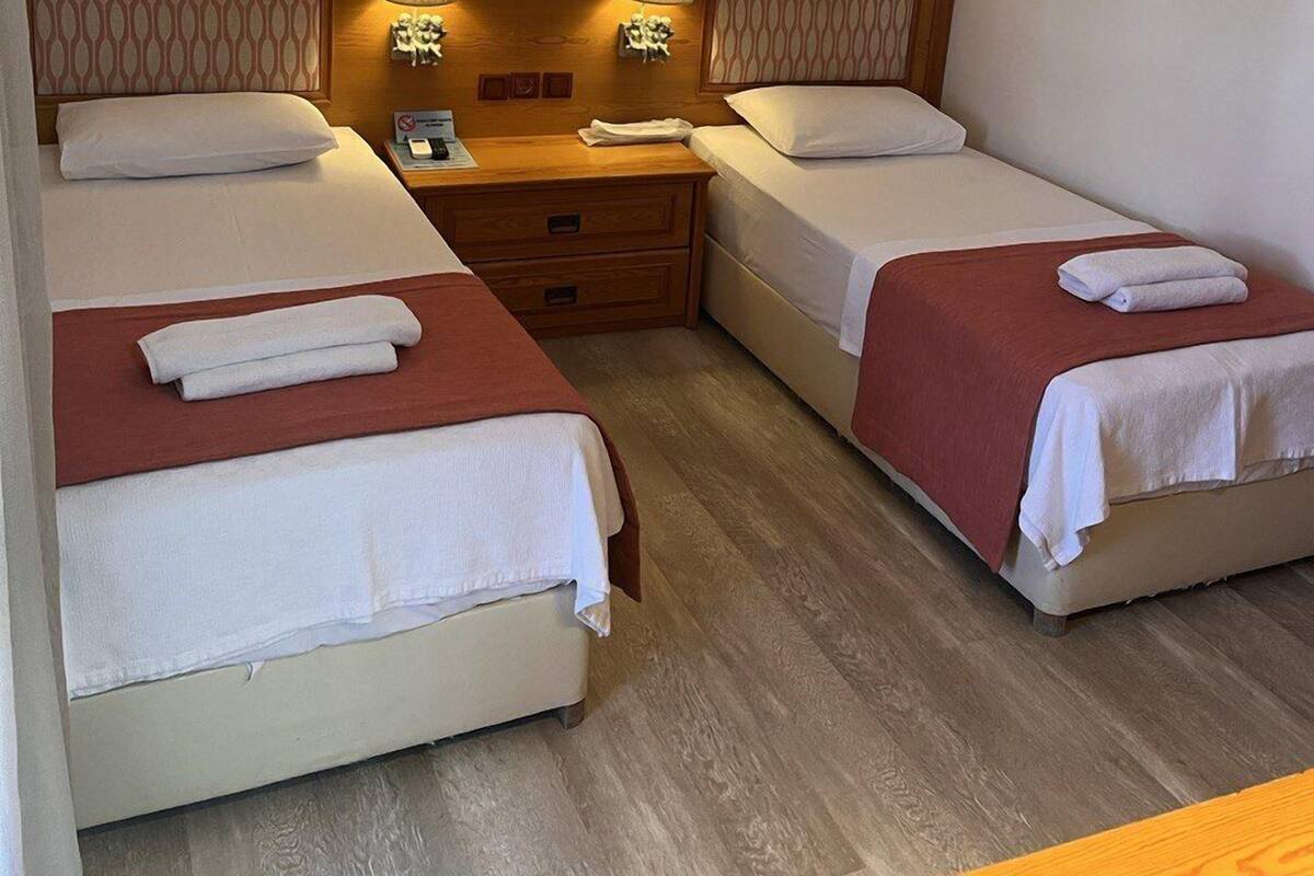 A hotel room with two beds, a wooden headboard, a nightstand, and an air conditioning unit.