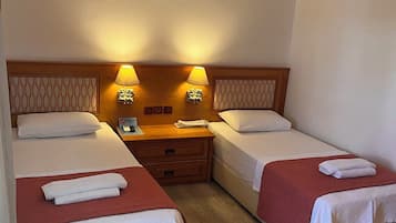 Habitación de hotel con dos camas, cabecera de madera, mesita de noche con lámpara y aire acondicionado.