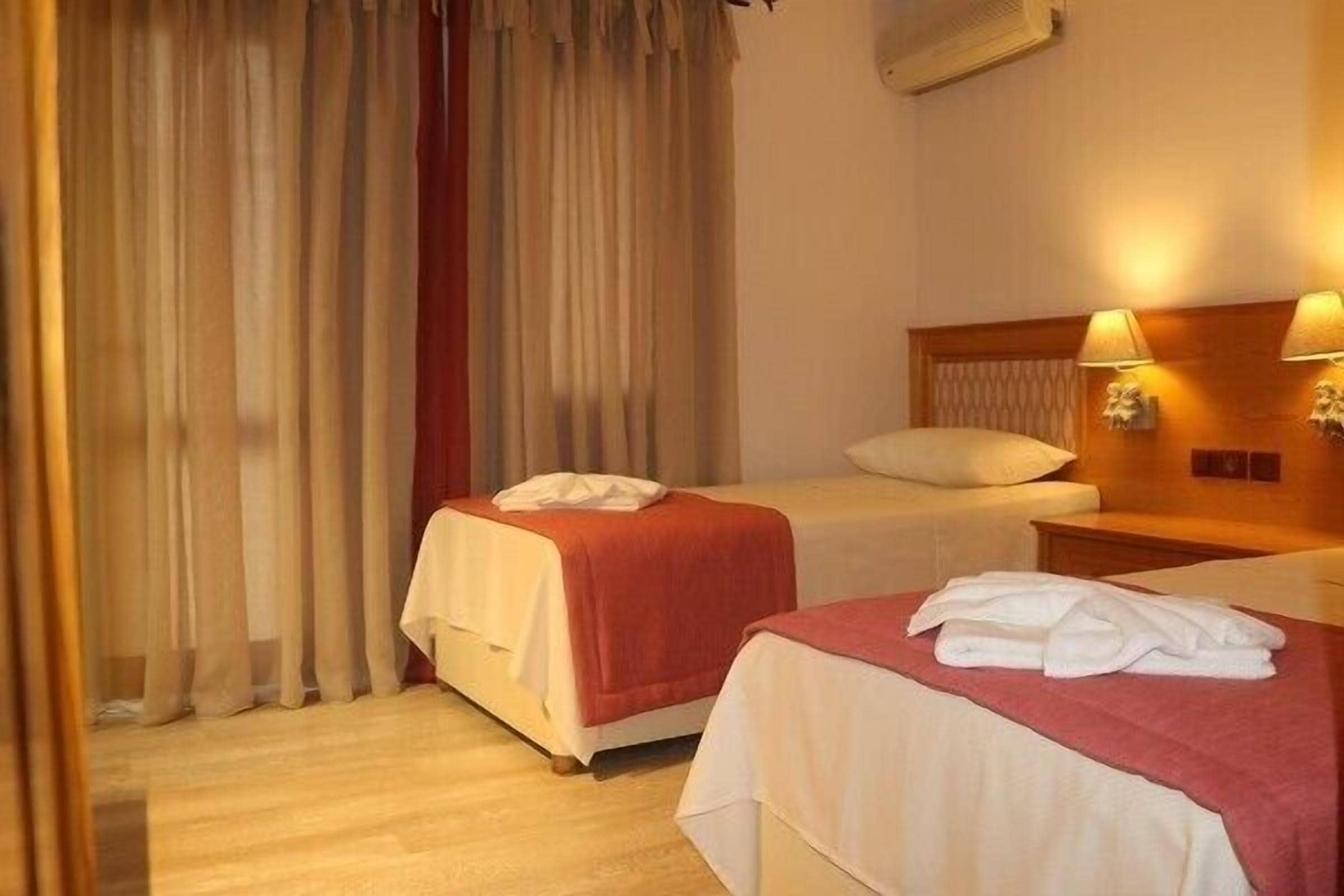 A hotel room with two beds, a wooden headboard, a nightstand, and a wall-mounted lamp.