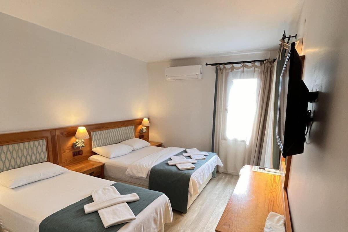 A hotel room with two beds, a wooden nightstand, a TV mounted on the wall, and an air conditioning unit.