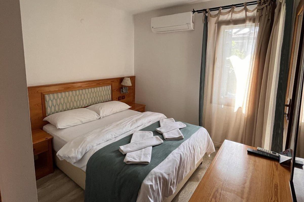 A bedroom with a wooden bed, a nightstand, a desk, and a window with curtains.