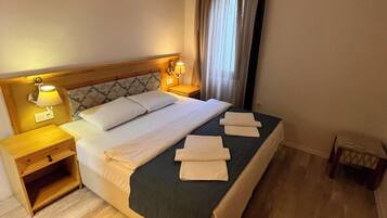 A hotel room with a bed, bedside tables, an air conditioning unit, and a window with curtains.