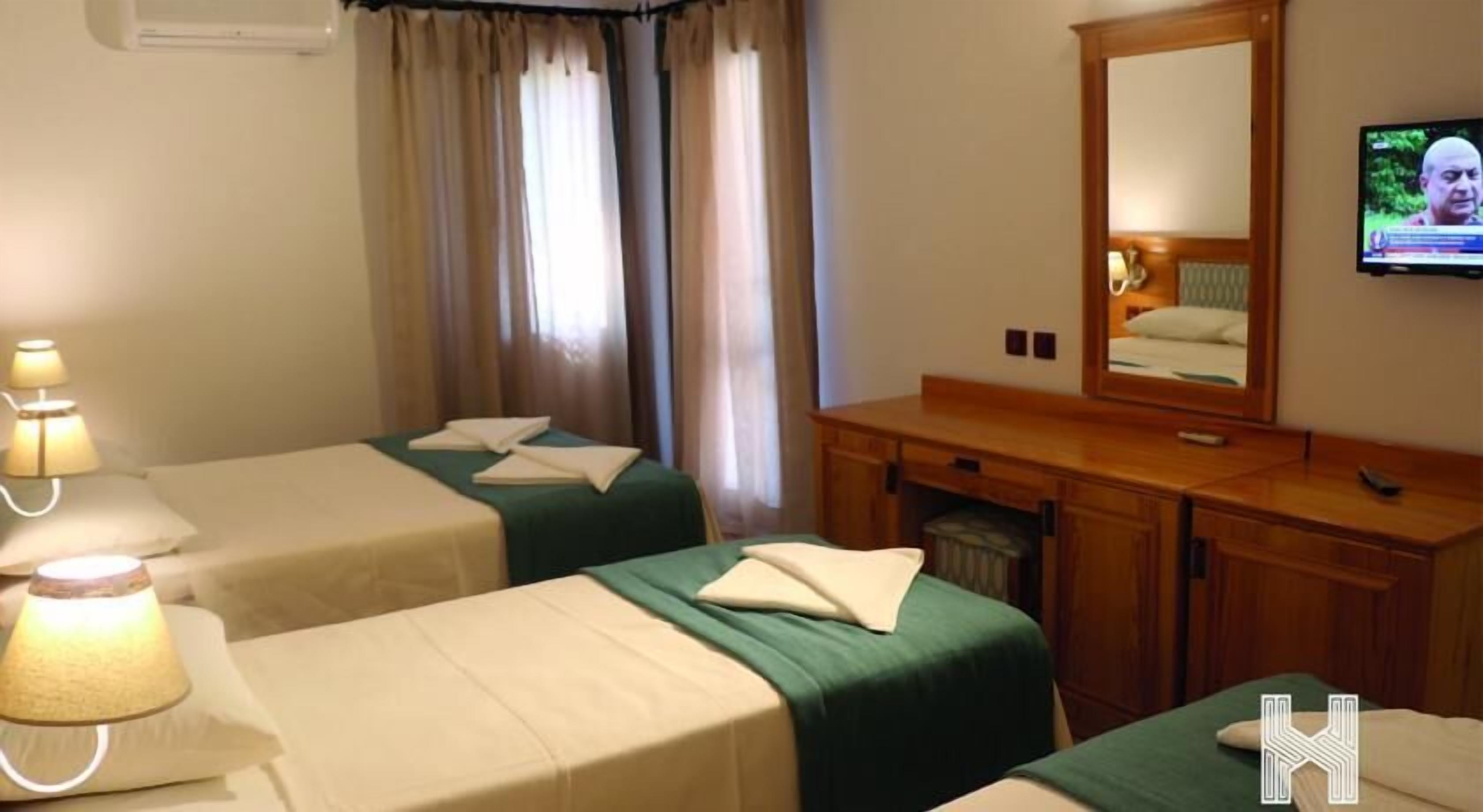 Habitación de hotel con dos camas, un aparador de madera, un televisor y una ventana con cortinas.