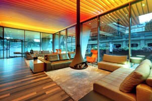 A modern interior with a large glass wall, a central fireplace, and a seating area with sofas and a coffee table.