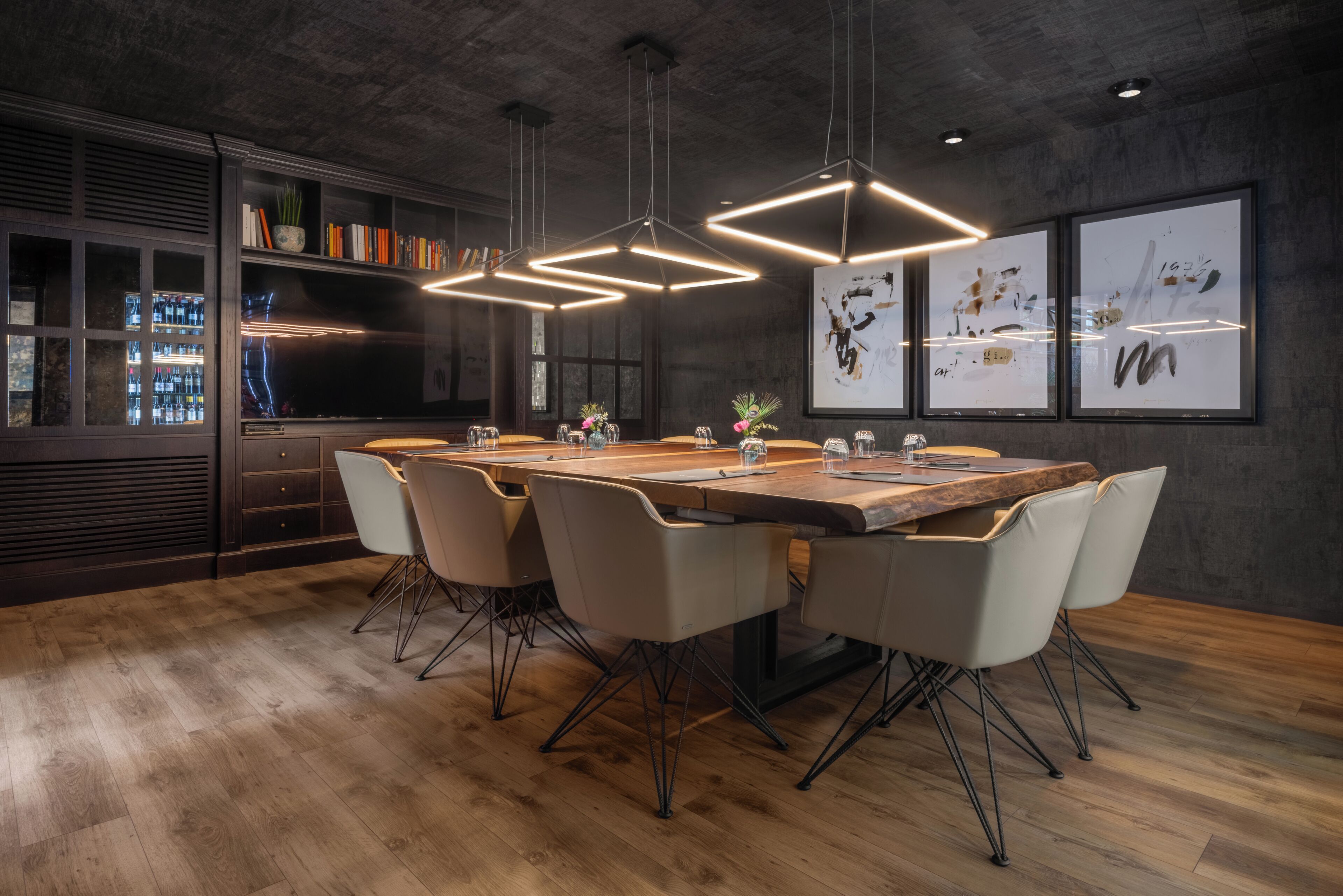 A modern dining area with a long wooden table, six chairs, pendant lights, and a bar area with shelves and a refrigerator.