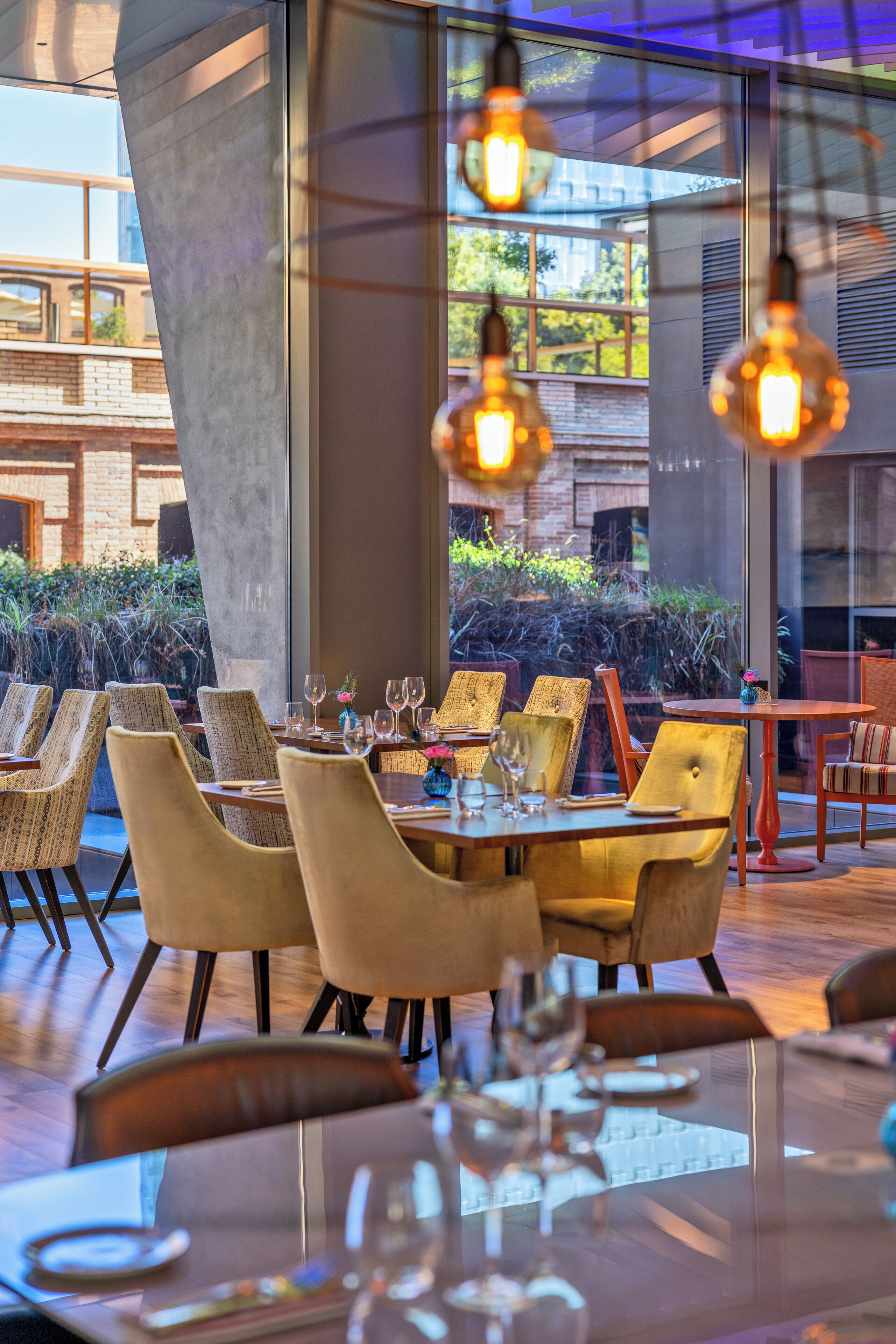 Un restaurant avec des tables et des chaises, de grandes fenêtres et des luminaires suspendus.