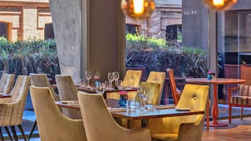 Un restaurante con mesas y sillas, ventanas amplias y lámparas colgantes.