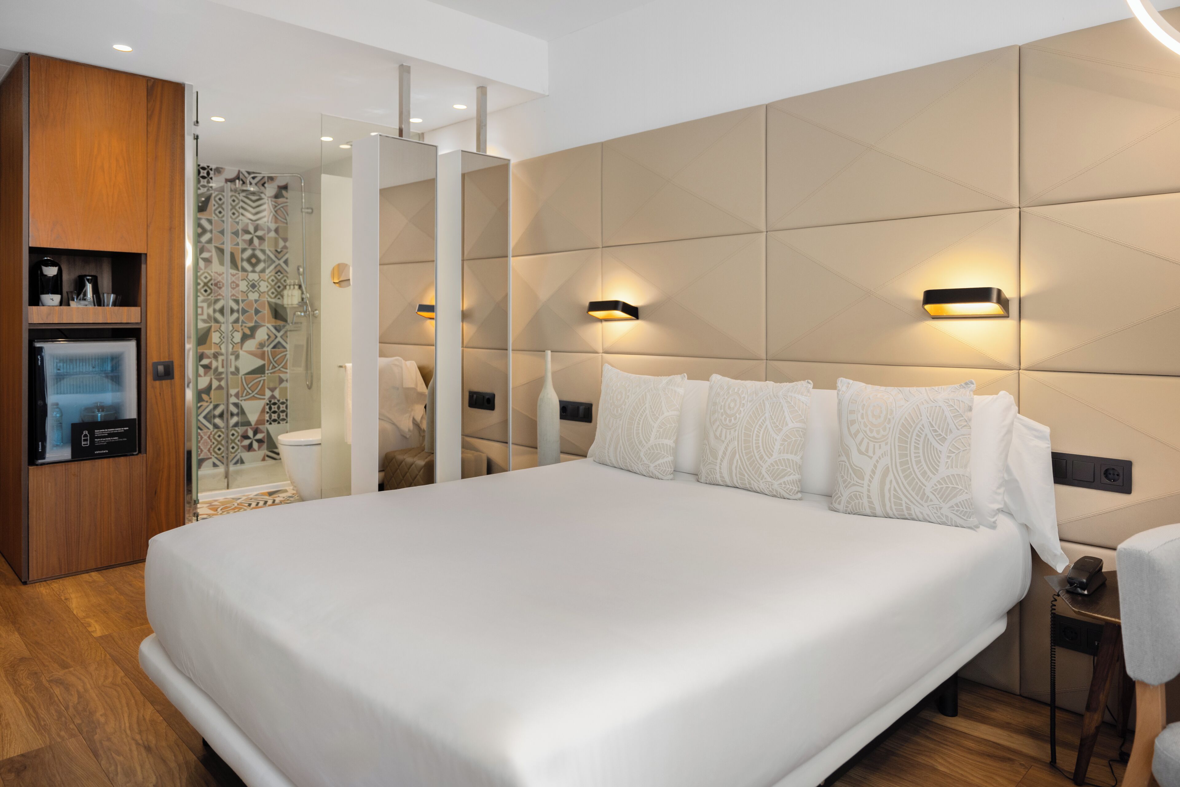 Una camera d'albergo moderna con un ampio letto, un armadio in legno, un angolo doccia e illuminazione a parete.
