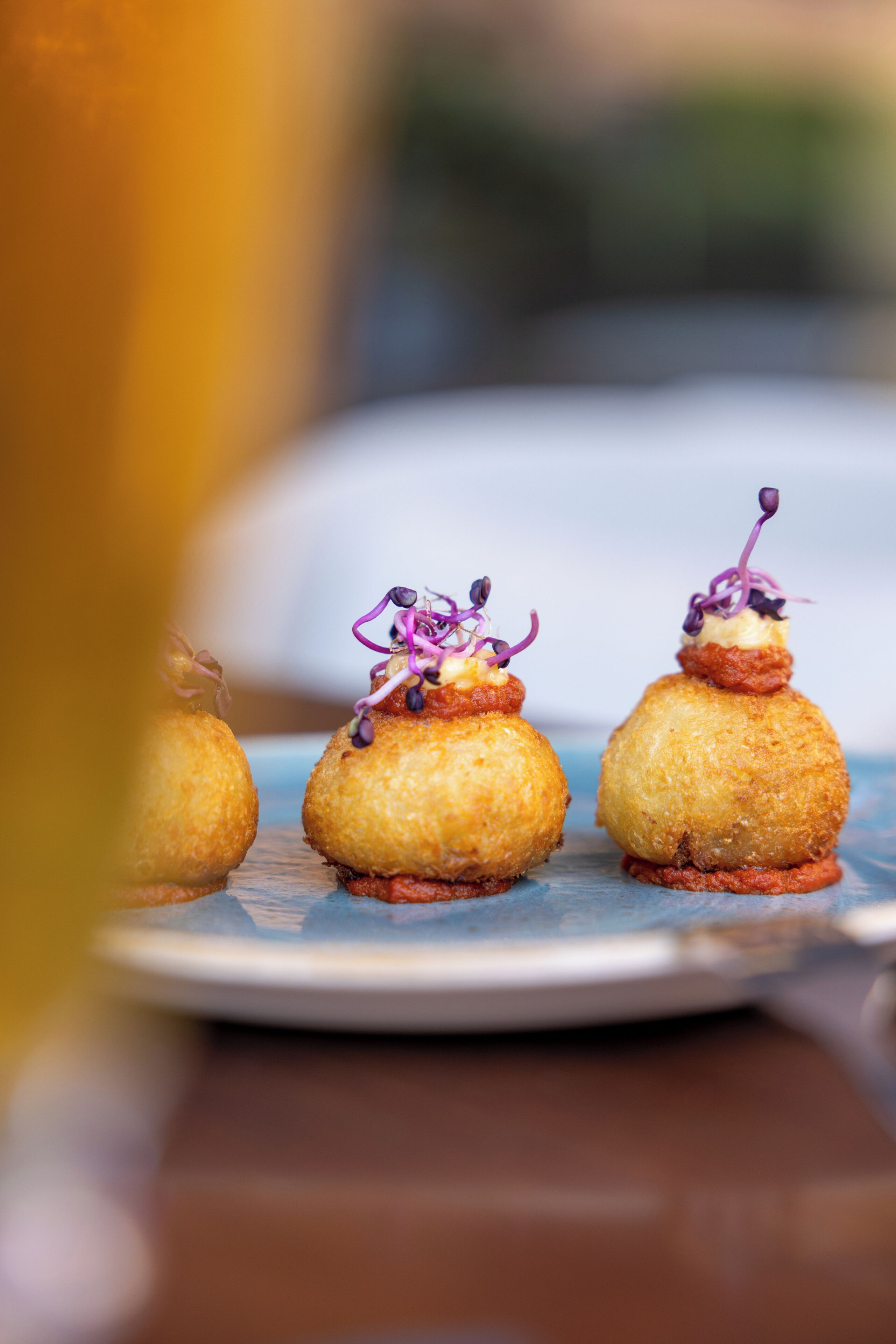 Un plato con tres aperitivos esféricos decorados con detalles morados, sobre una superficie azul.