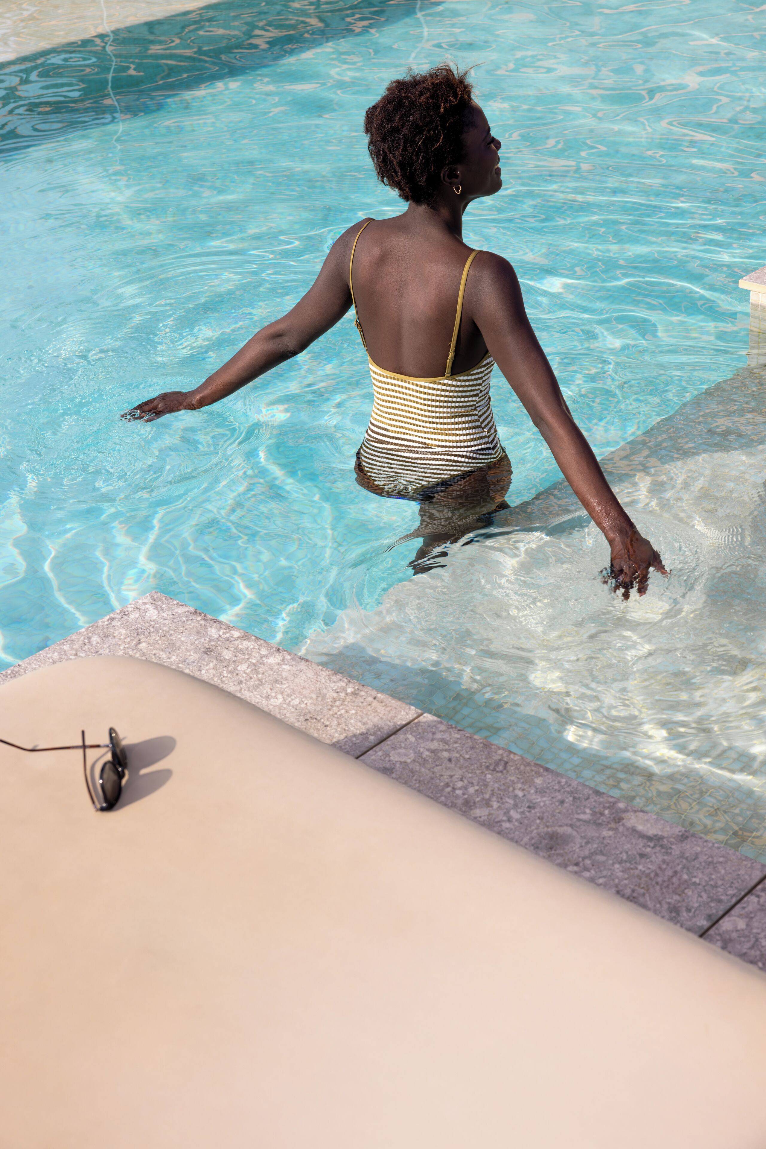 Une personne se trouve dans une piscine, avec une vue dégagée sur le bord du bassin et une chaise longue à proximité.