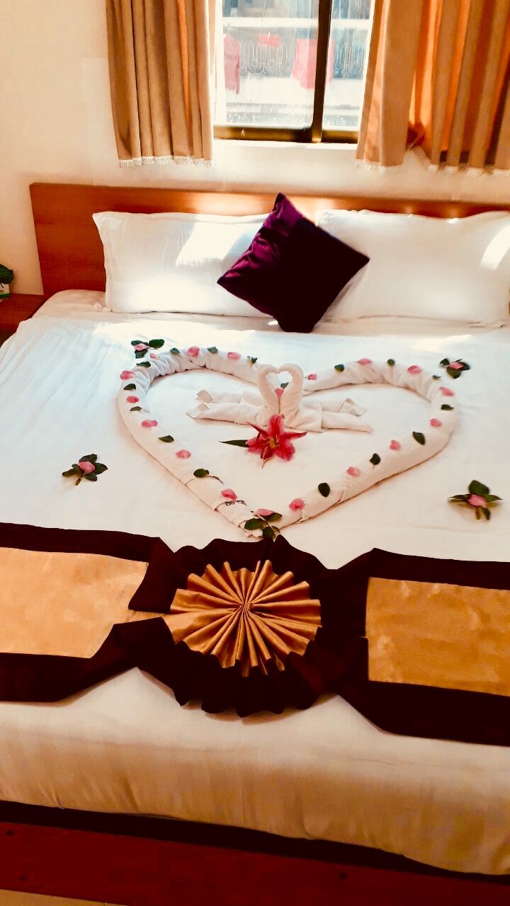 A bed with a heart-shaped towel arrangement, a purple pillow, and a decorative item on the bedspread.