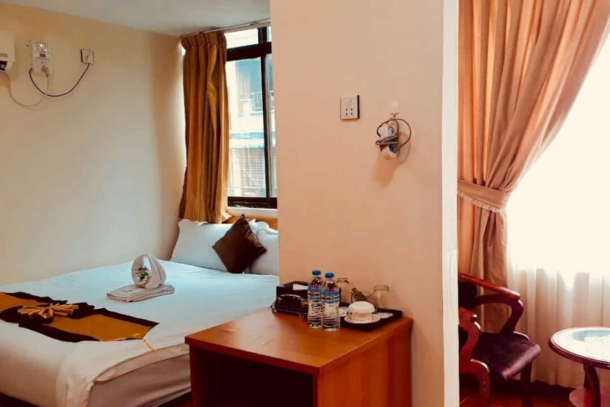 Una habitación de hotel con cama, mesita de noche, silla y una pequeña mesa junto a la ventana.
