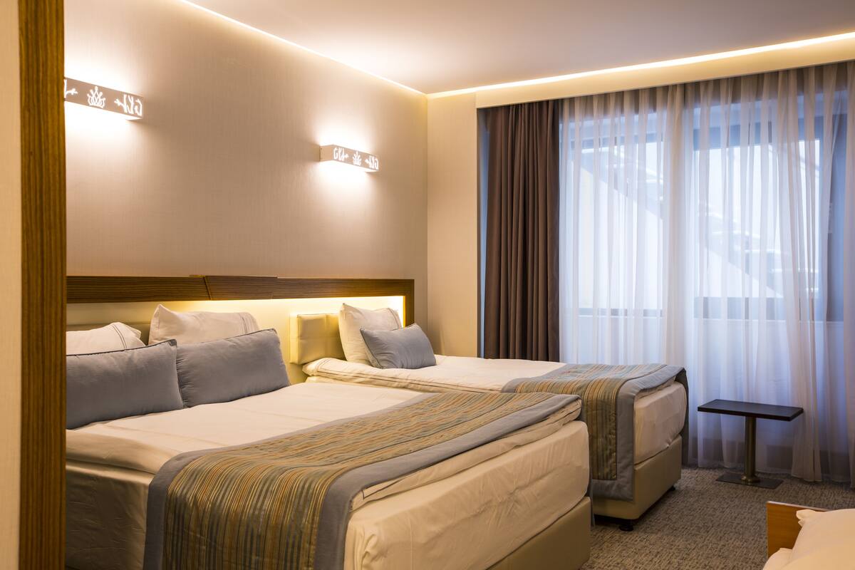 A hotel room with two beds, a small table, and a large window with curtains.