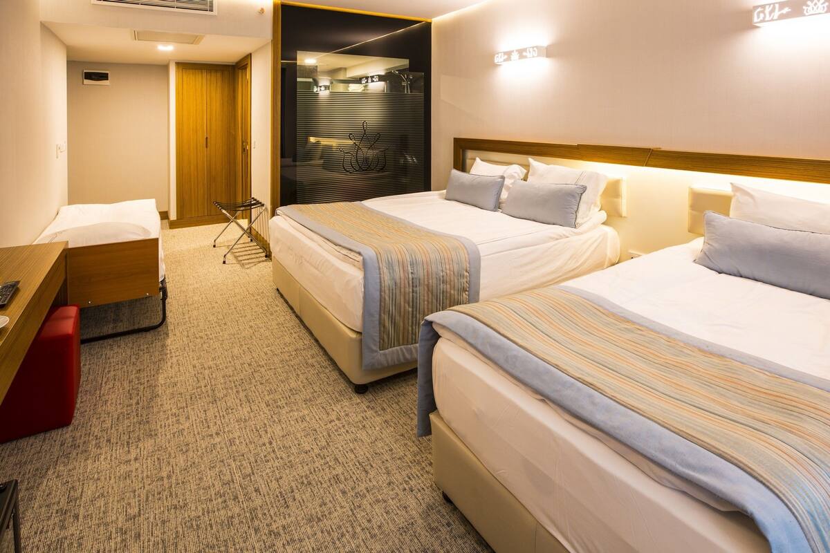 A hotel room with two beds, a desk, and a red bench.