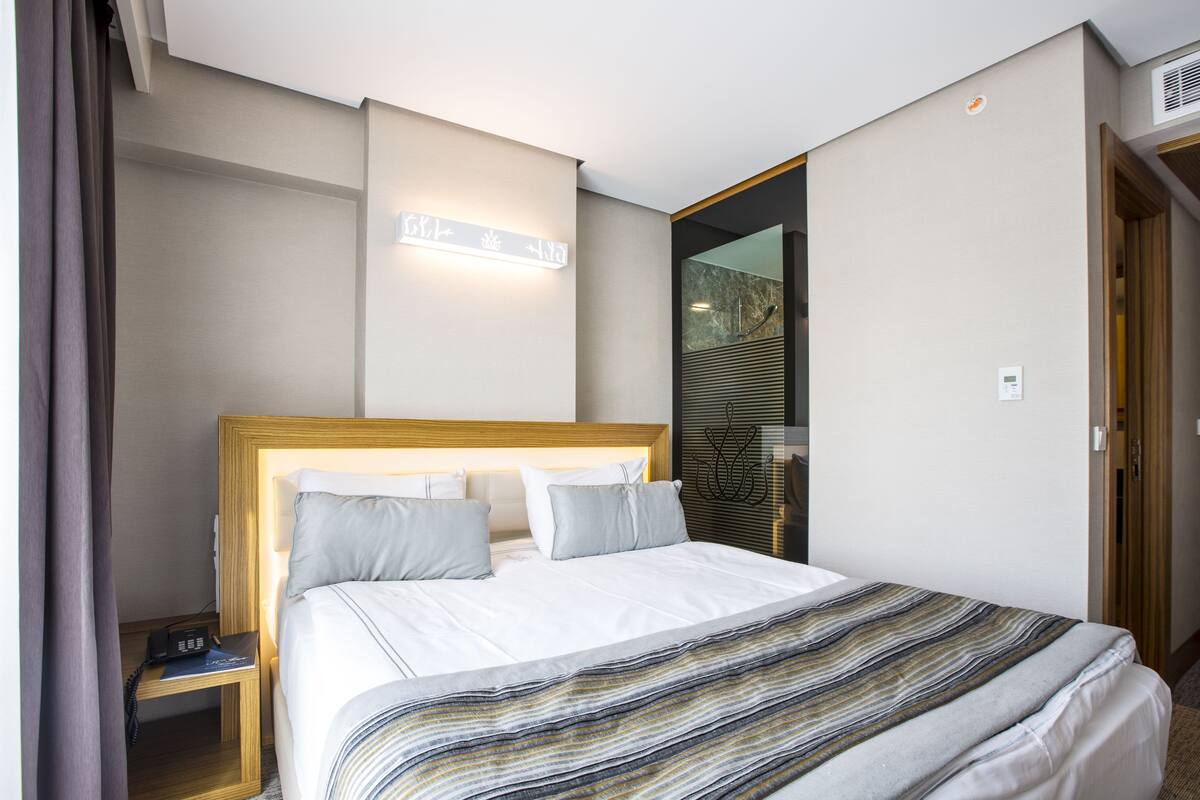 A hotel room with a large bed, a bedside table, a nightstand, a wall-mounted light, and a mirror.