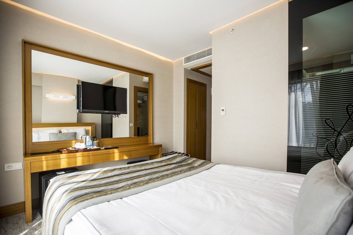 A modern hotel room with a large bed, a flat-screen TV, a wooden dresser, and a large mirror.