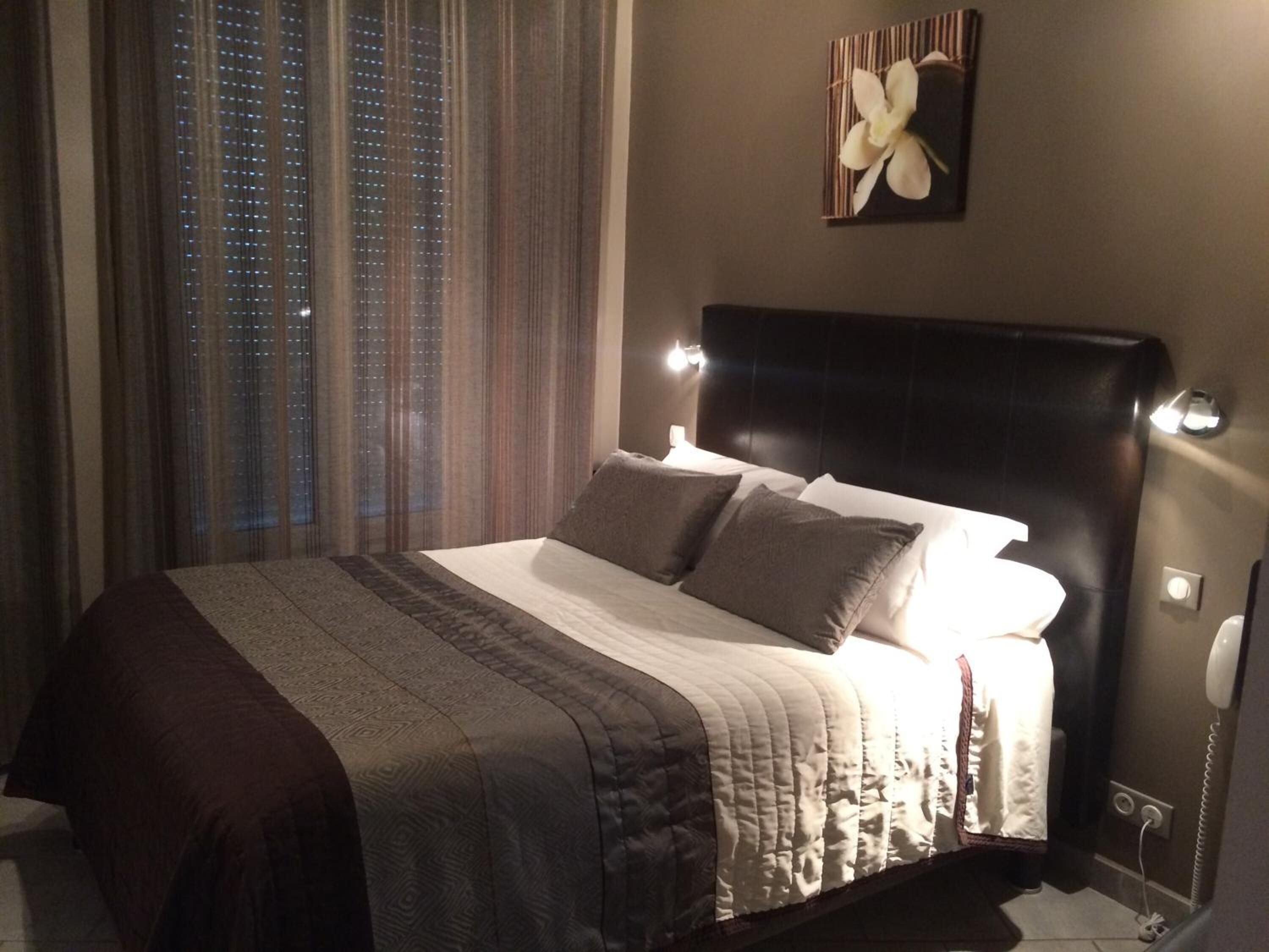 Una habitación de hotel con una cama grande, un cabecero oscuro y una ventana con cortinas.