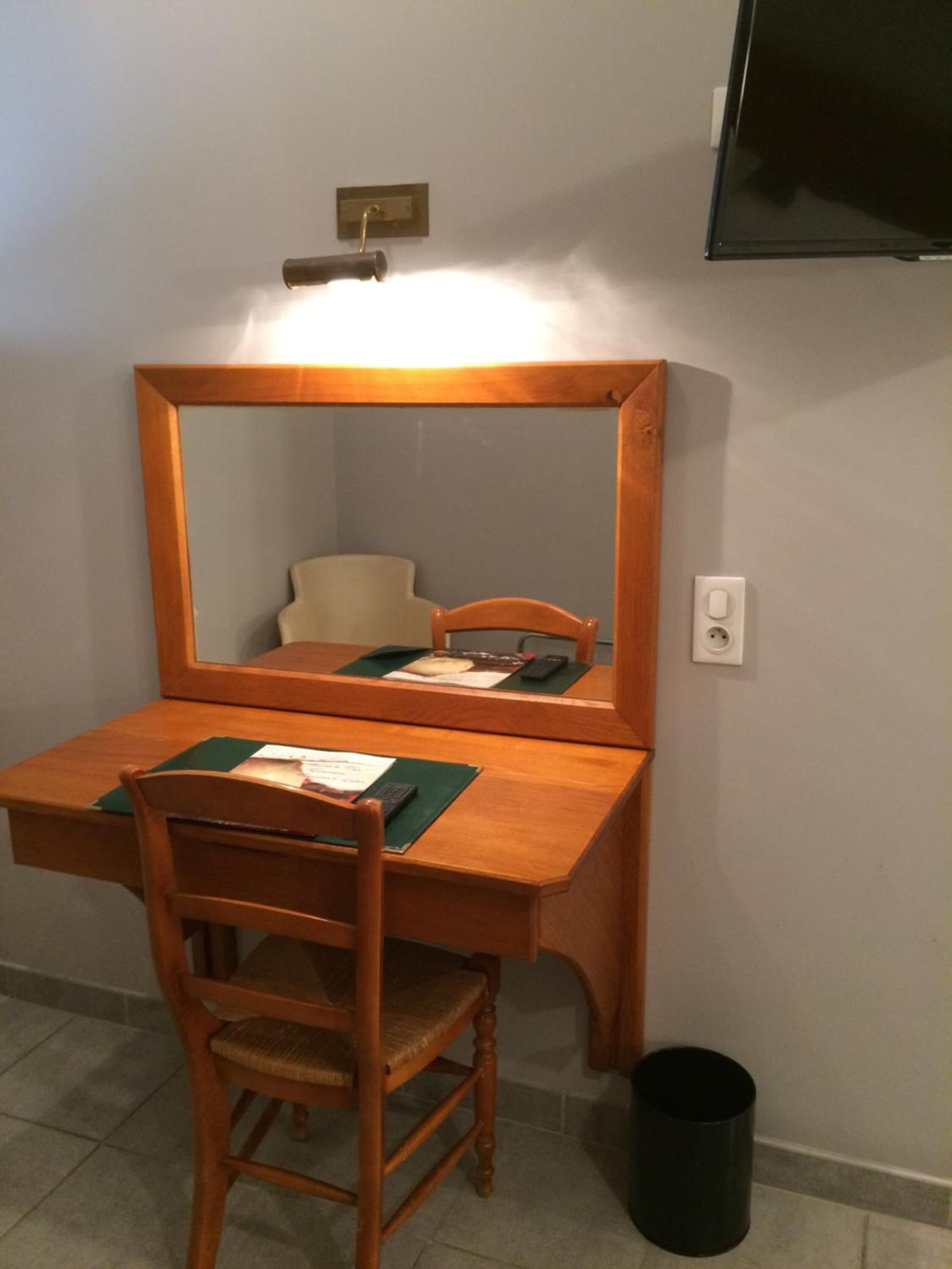 Un escritorio de madera con un espejo, una silla y un pequeño cubo de basura.