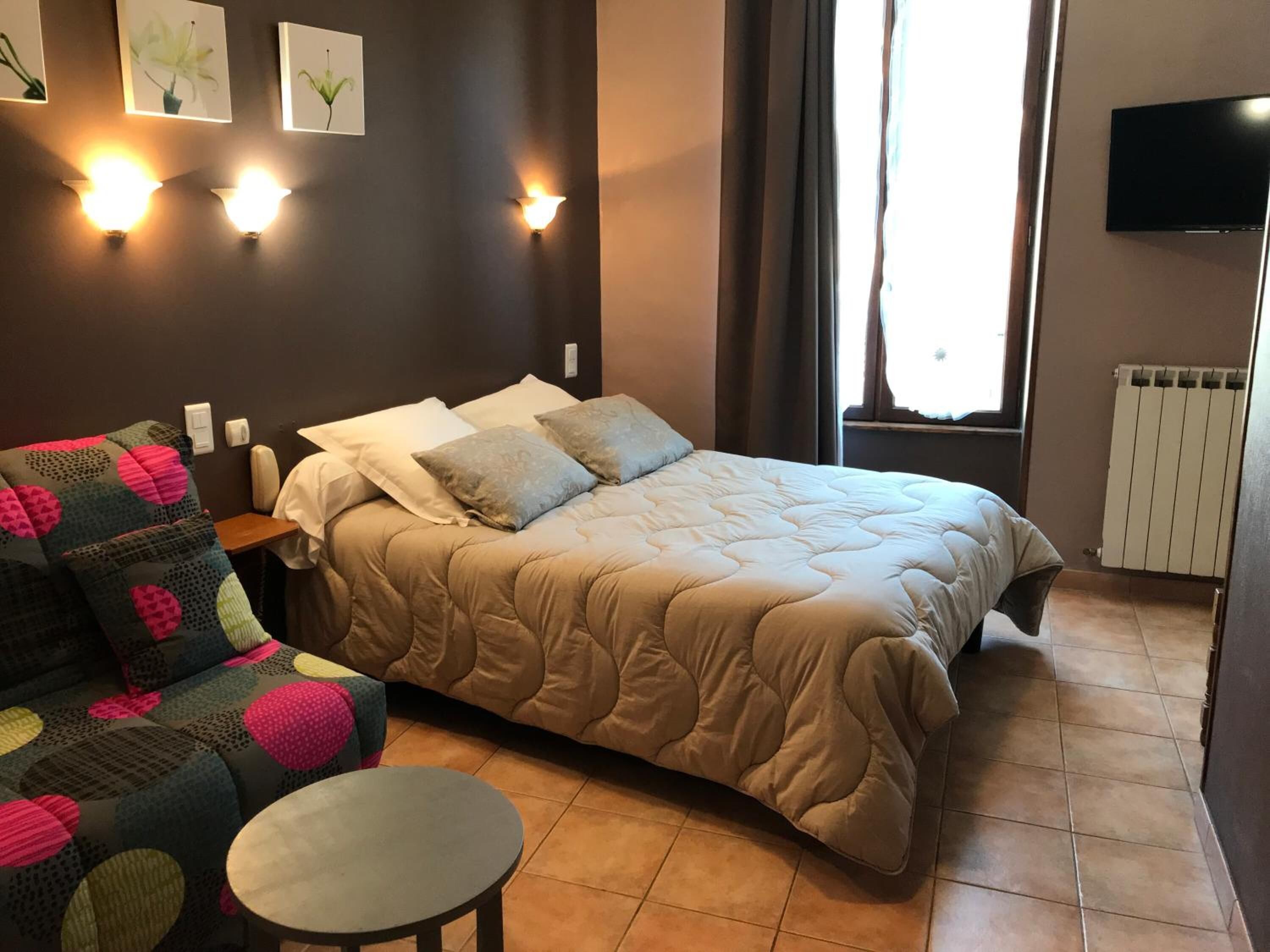 Een slaapkamer met een bed, een slaapbank, een klein tafeltje en wandlampen.
