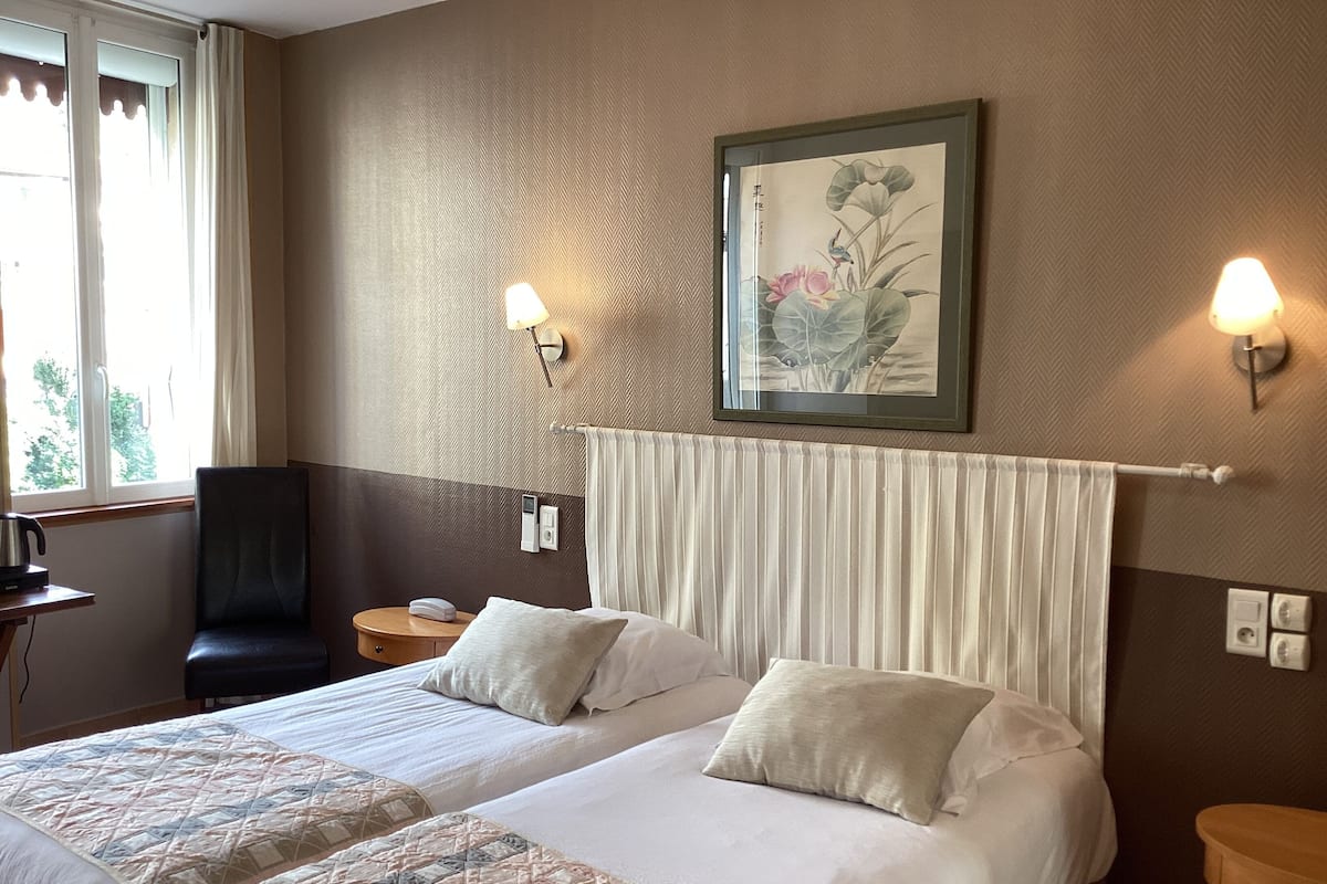 A hotel room with two beds, a chair, a desk, and a wall-mounted painting.