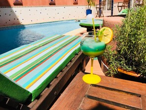 Zona de piscina con una silla de descanso a rayas, una bebida con rodaja de limón y una planta en maceta.