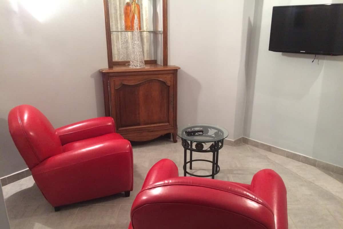 A living room with two red leather chairs, a small glass table, a wooden cabinet, and a flat-screen TV mounted on the wall.