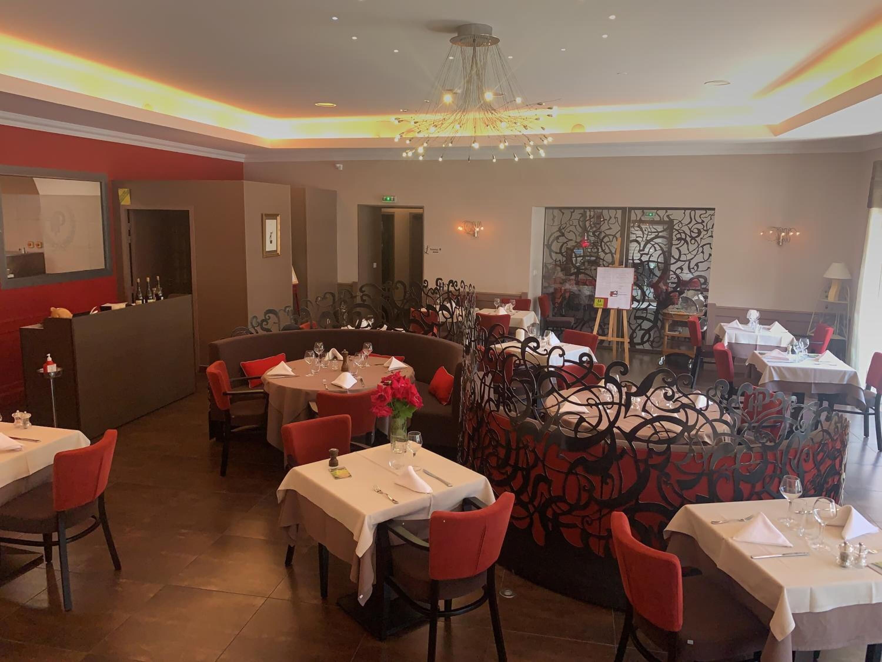 Restaurante com mesas redondas, cadeiras vermelhas e uma parede decorativa.