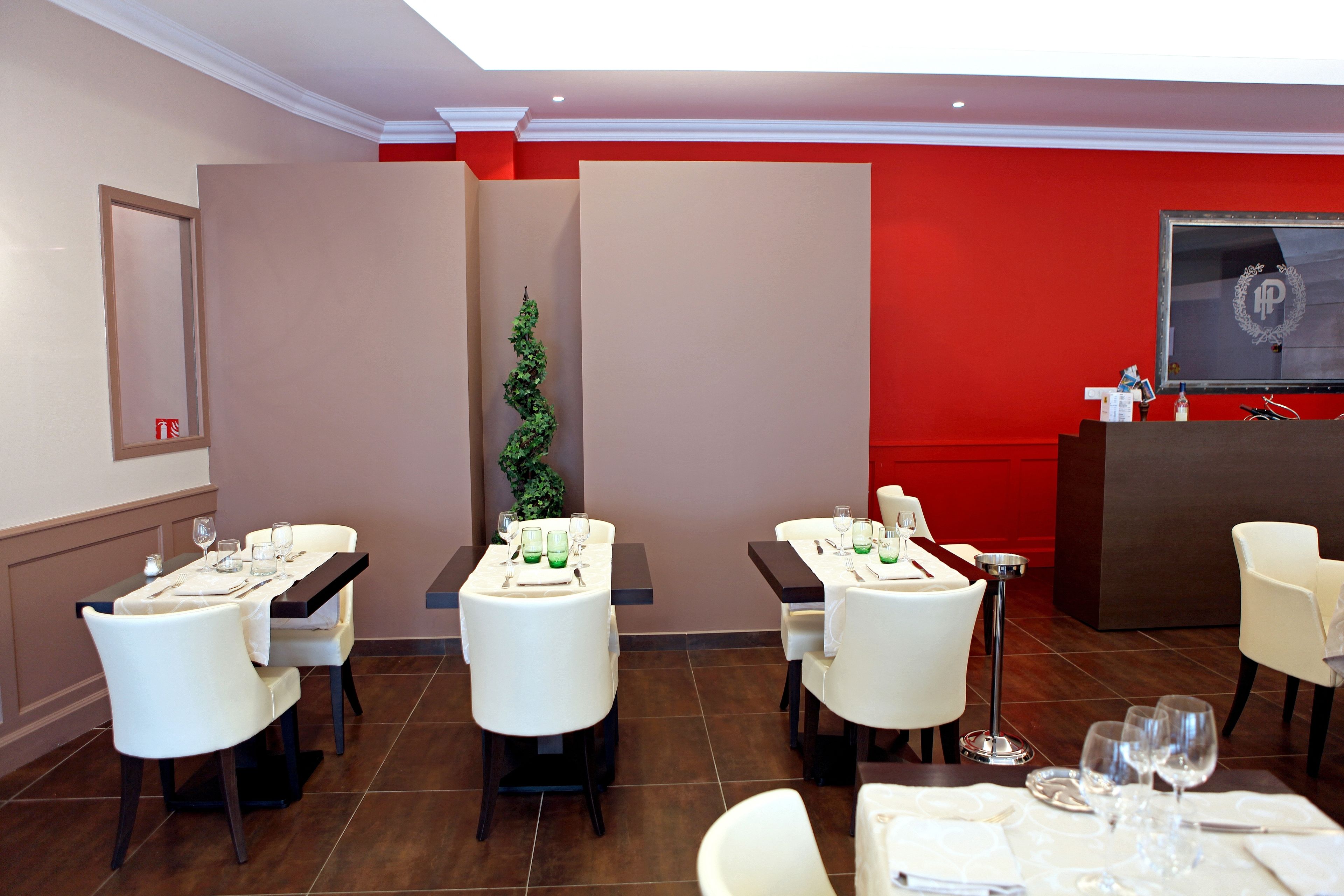 Comedor de hotel con mesas dispuestas para cuatro, sillas blancas, pared de acento roja y una pantalla grande mostrando un logotipo.