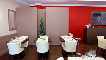 Comedor de hotel con mesas dispuestas para cuatro, sillas blancas, pared de acento roja y una pantalla grande mostrando un logotipo.